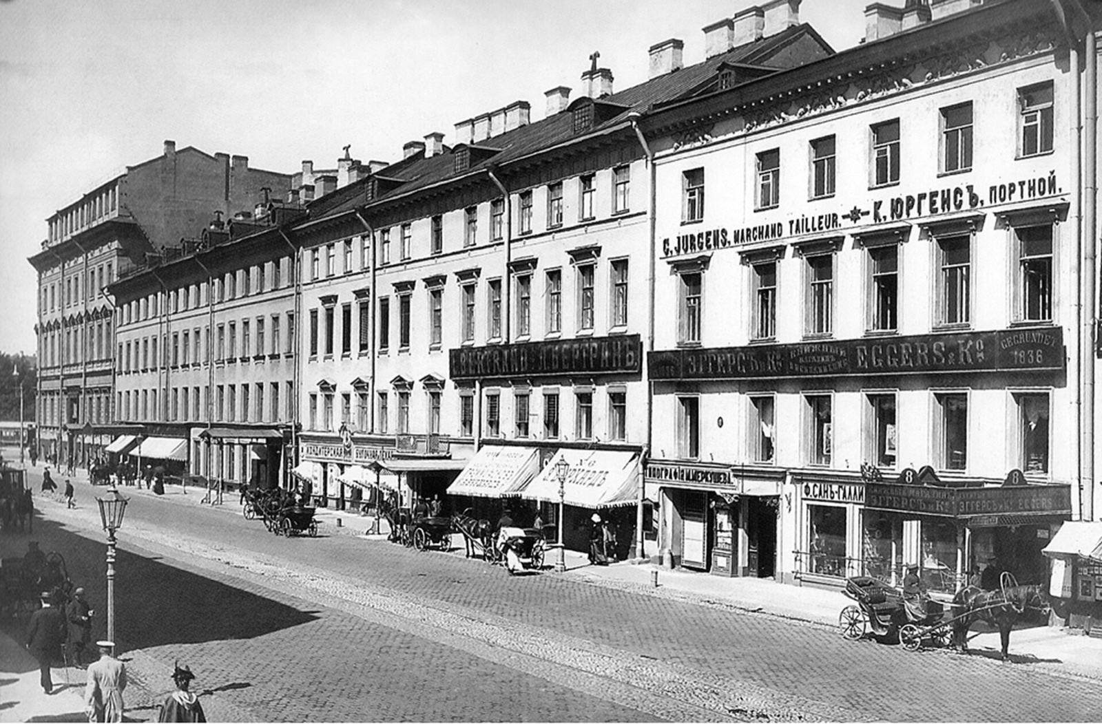 Чёрно-белая фотография Невского проспекта начала XX века: фасады домов 2–8 с вывесками портного, магазинов и контор, на мостовой извозчики